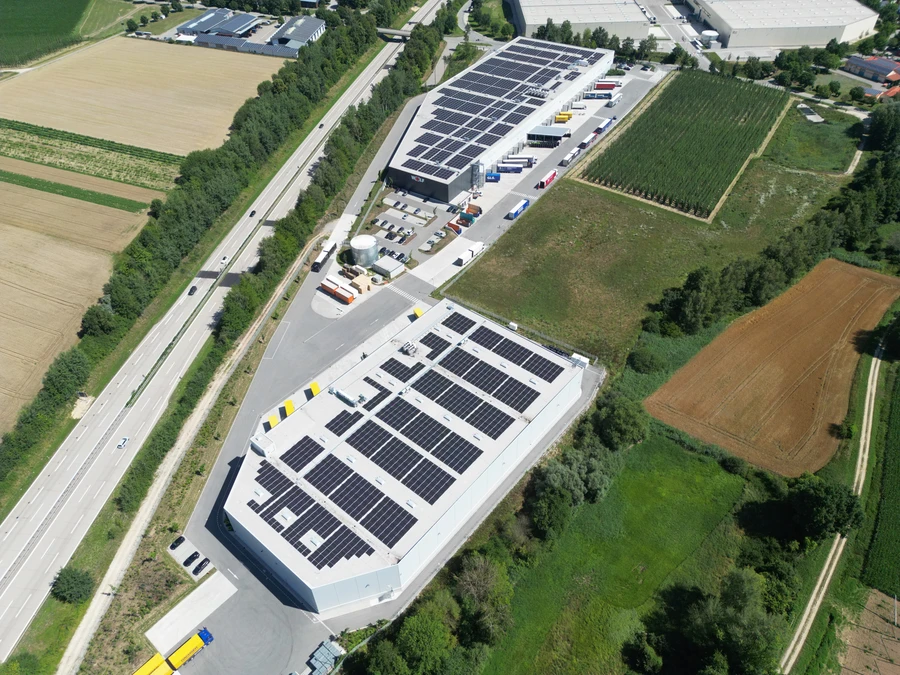 Luftaufnahme des Logistikzentrums in Siegenburg mit den Dach-PV-Anlagen auf zwei Lagerhallen und dem Lkw-Verladehof davor.