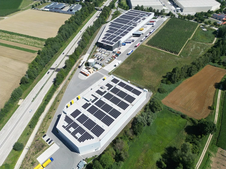 Luftaufnahme des Logistikzentrums in Siegenburg mit den Dach-PV-Anlagen auf zwei Lagerhallen und dem Lkw-Verladehof davor.