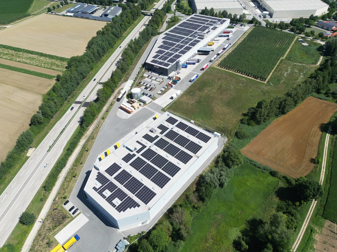 Luftaufnahme des Logistikzentrums in Siegenburg mit den Dach-PV-Anlagen auf zwei Lagerhallen und dem Lkw-Verladehof davor.